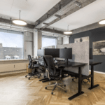 Modern open-plan office with ergonomic chairs, dual monitors, and natural lighting.