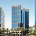 Modern glass office buildings with palm trees in front under a clear blue sky in a business district