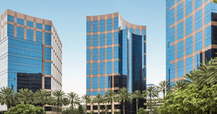 Modern glass office buildings with palm trees in front under a clear blue sky in a business district