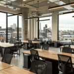 Open-plan office with wooden desks, ergonomic chairs, city views, and floor-to-ceiling windows