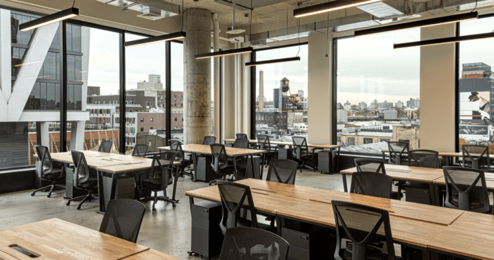 Open-plan office with wooden desks, ergonomic chairs, city views, and floor-to-ceiling windows